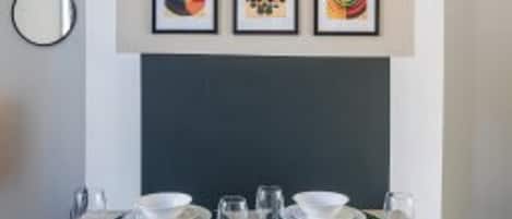 Ein Essbereich mit einem Tisch für vier Personen, Kunstwerken darüber und einem runden Spiegel an der Wand.