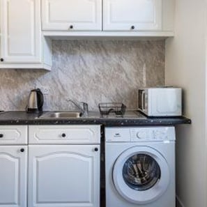 A kitchen with white cabinets, a washing machine, a kettle, and a toaster. - Gateshead - Stay5 - Free Parking - Transport Links (Gateshead)