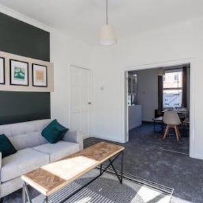 A living room with a sofa, a coffee table, and a door leading to another room. - Gateshead - Stay5 - Free Parking - Transport Links (Gateshead)