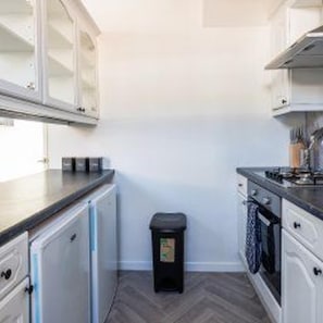 A compact kitchen with white cabinets, a black trash bin, and a herringbone-patterned floor. - Gateshead - Stay5 - Free Parking - Transport Links (Gateshead)