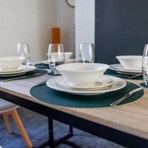 A dining table set with plates, bowls, and glasses, with a dark green placemat. - Gateshead - Stay5 - Free Parking - Transport Links (Gateshead)