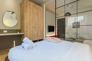 A modern hotel room with a large bed, a wooden wardrobe, a flat-screen TV, and a glass wall offering a view of the outside. - Pasteur 627 Gemmayze by Stayinn (Beirut)