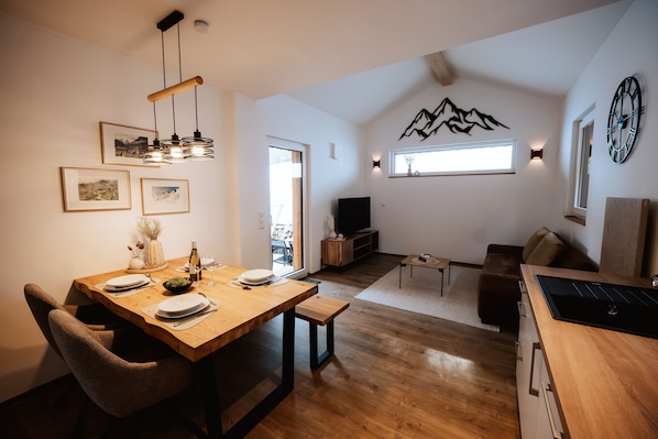 A modern living space with a dining area, a sofa, a TV, and a kitchen area.