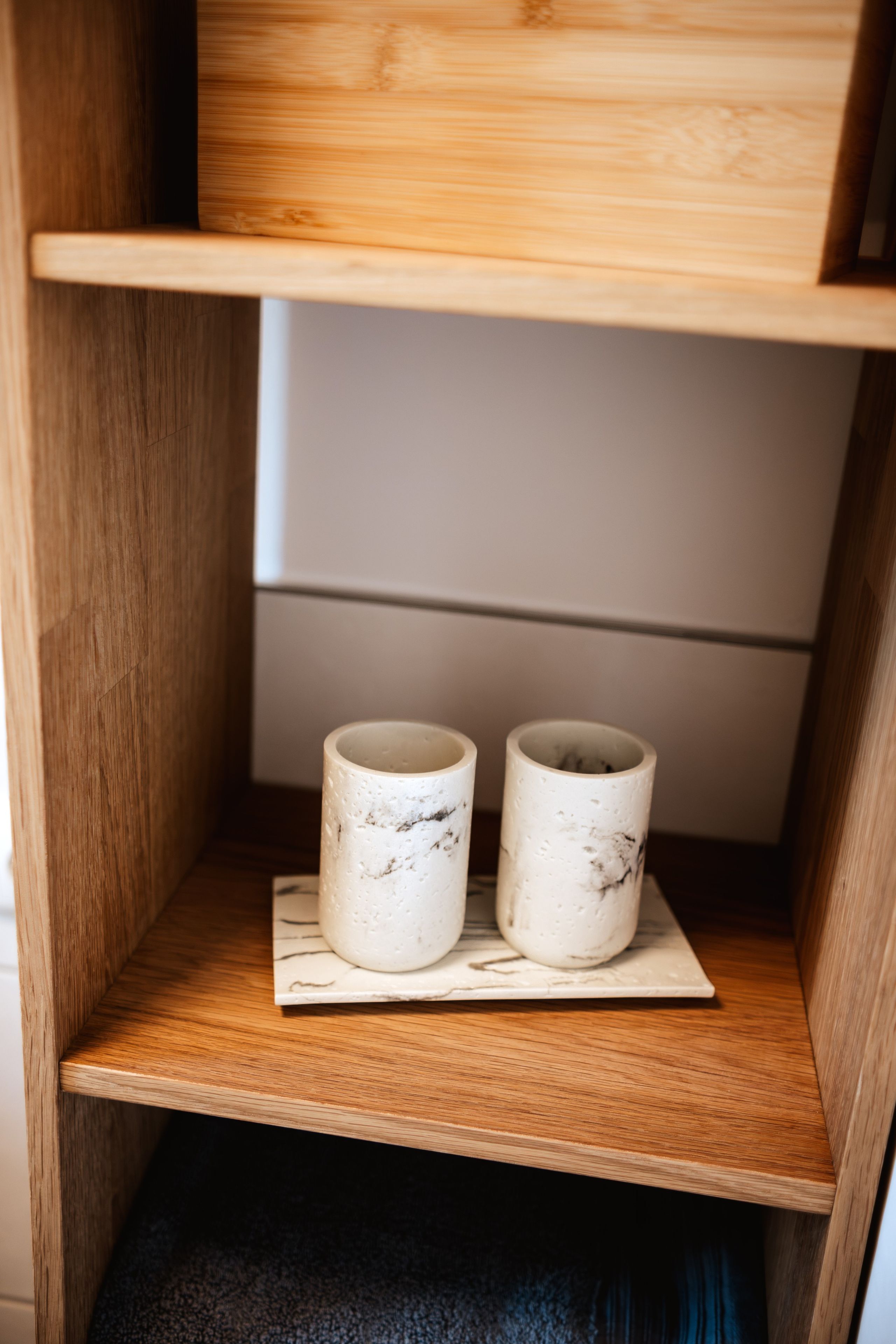 Une étagère en bois sur laquelle reposent deux tasses en céramique blanche, posées sur un sous-verre à motifs de marbre.