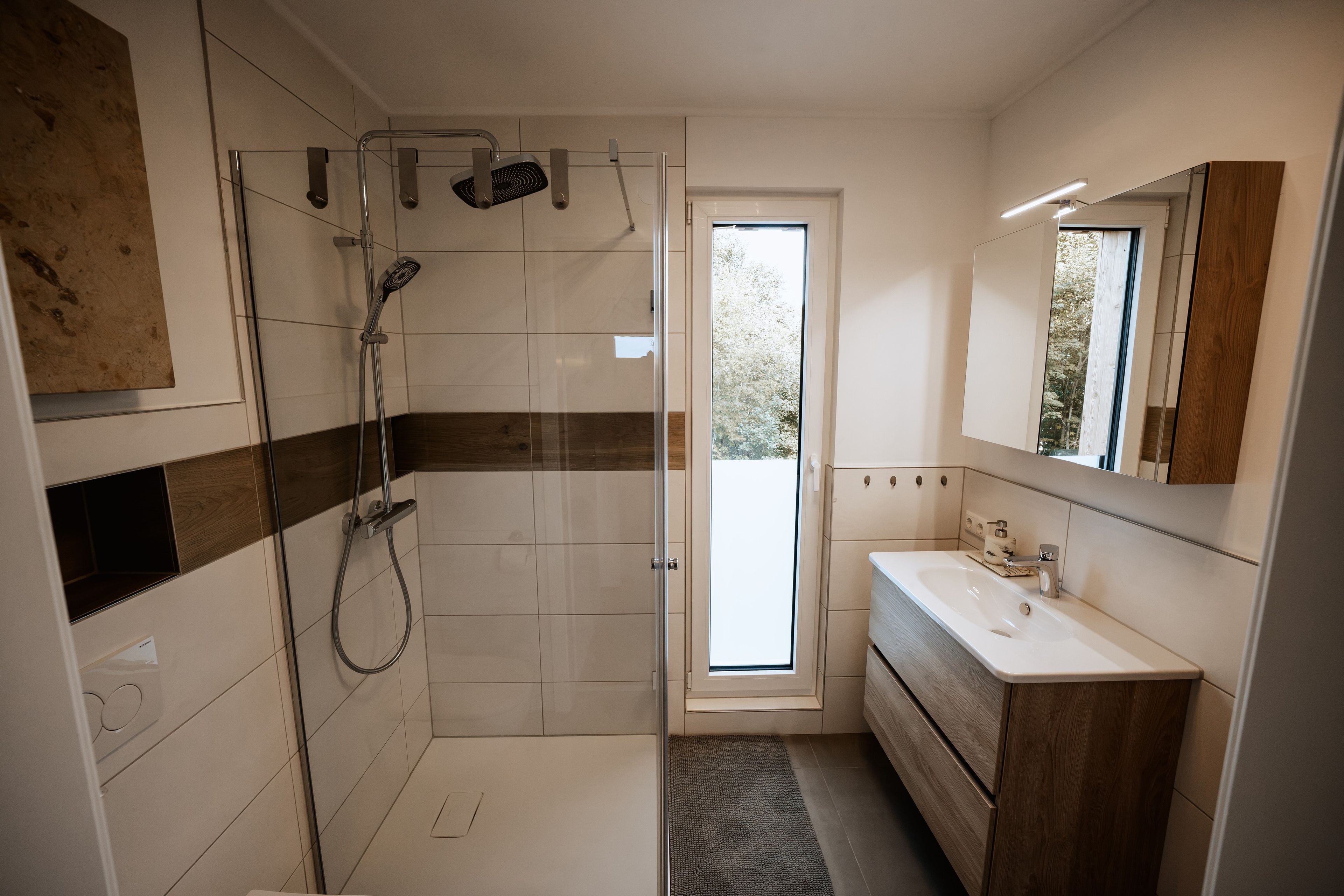 Ein modernes Badezimmer mit Duschkabine aus Glas, einem Holzbadezimmerhocker und einem großen Spiegel.