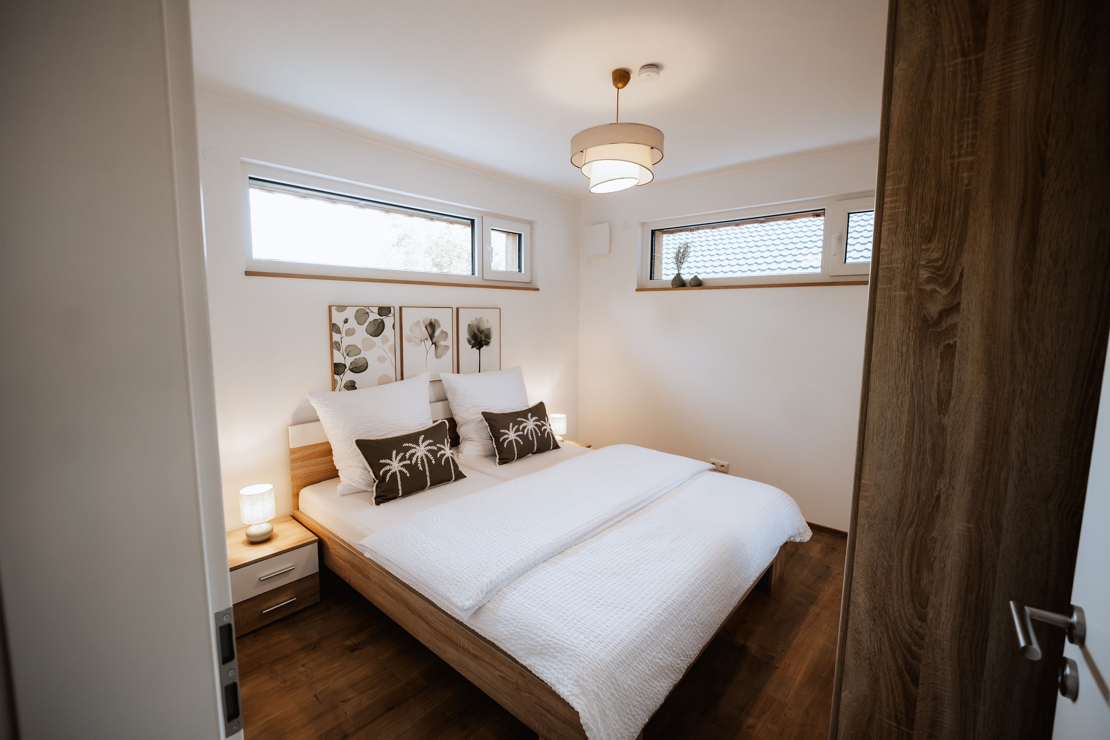 Een slaapkamer met een bed, nachtkastjes, een raam en een plafondlamp.