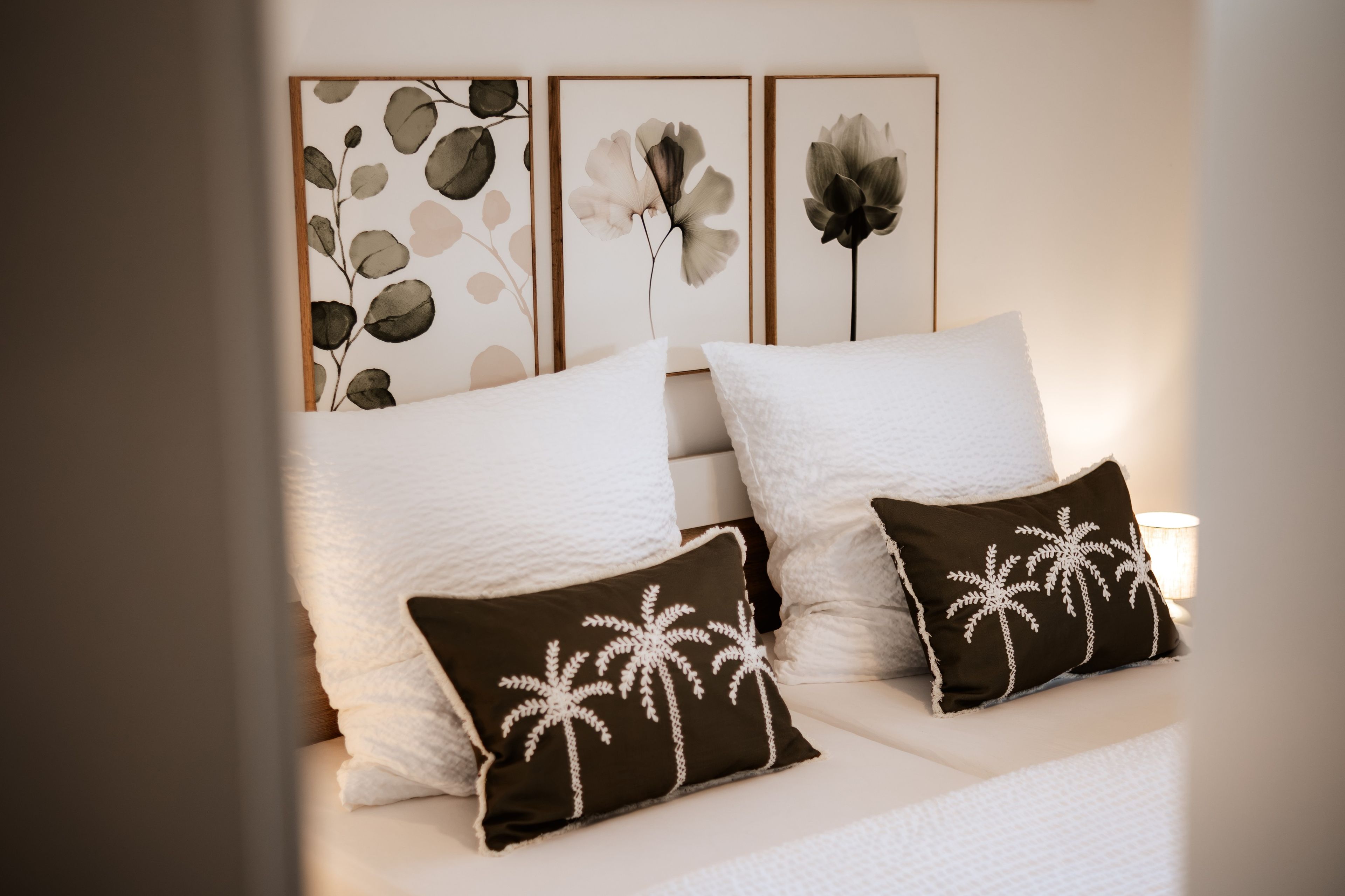 A neatly made bed with white bedding and two decorative pillows with palm tree designs.
