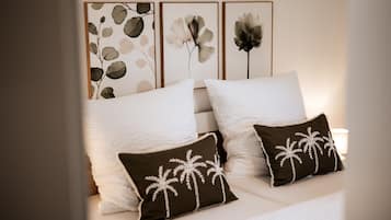 A neatly made bed with white bedding and two decorative pillows with palm tree designs.