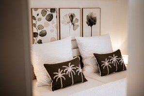 A neatly made bed with white bedding and two decorative pillows with palm tree designs.