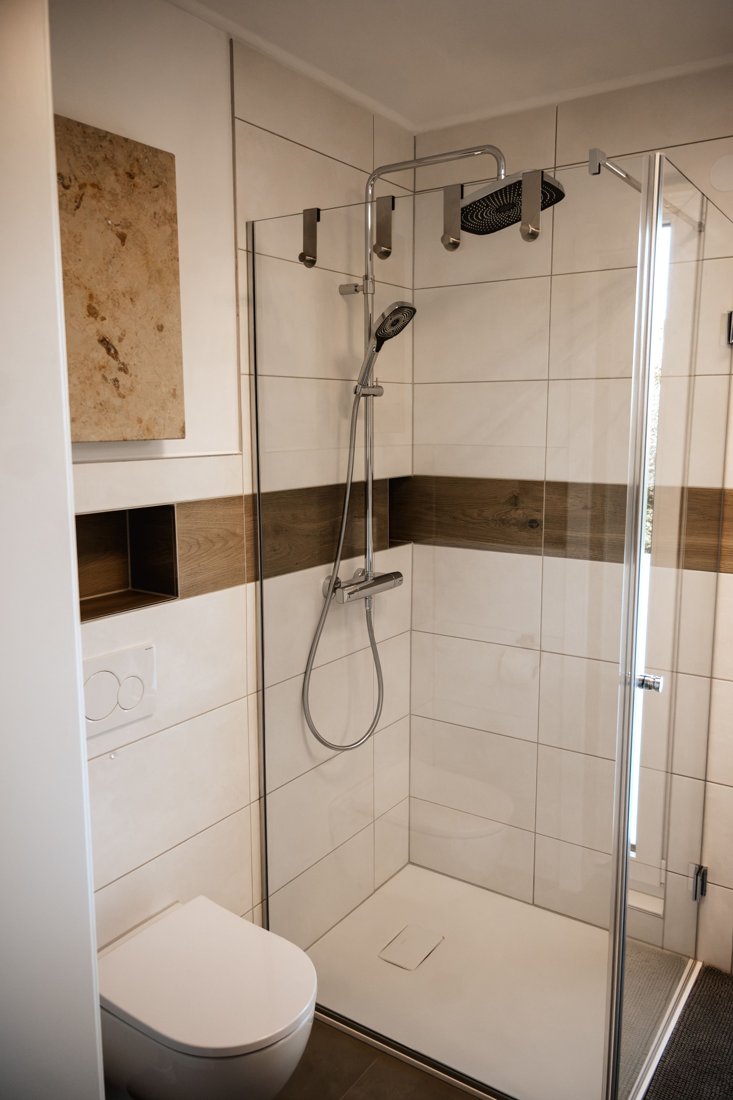 Eine moderne Duschkabine mit Glastür, Handbrause und Kopfbrause.