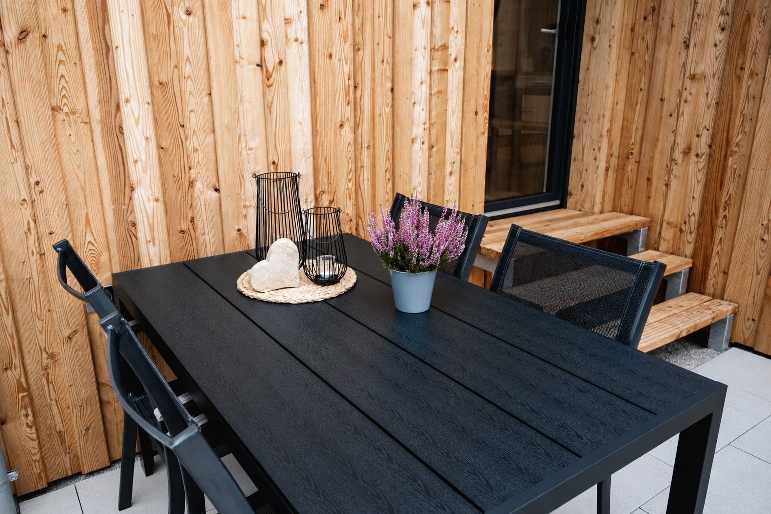 A wooden dining table with chairs, a black tablecloth, and a potted plant with purple flowers.