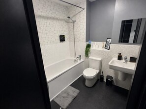 A modern bathroom with a bathtub, toilet, and sink. - Oak & Noir 2 Bed 2 Bath Wifi Free Parking Near Uni (Manchester)