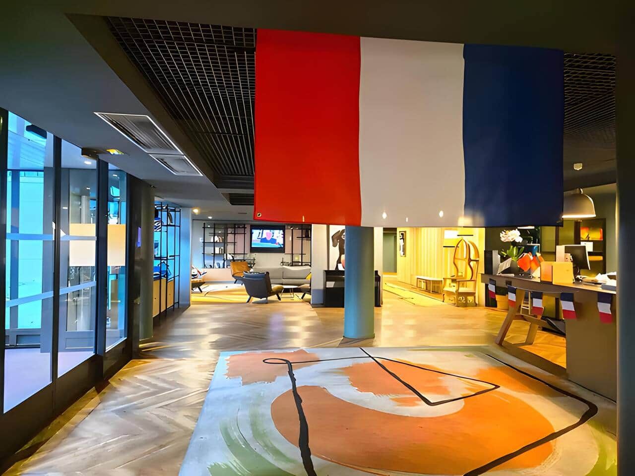 A spacious lobby with a modern design, featuring a large open area with a patterned floor, a reception desk, and a seating area with a television.