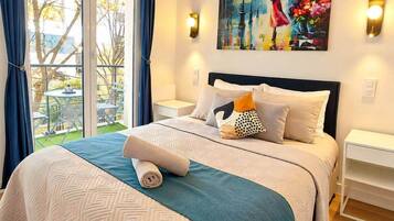 A hotel room with a large bed, a painting on the wall, and a view of the outdoors.