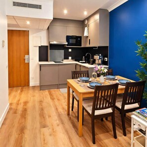 A compact kitchen with modern appliances, a dining area with a wooden table and chairs, and a blue accent wall. - Paris Expo 5 min – Cozy 1BR Apt with Balcony (Issy-les-Moulineaux)