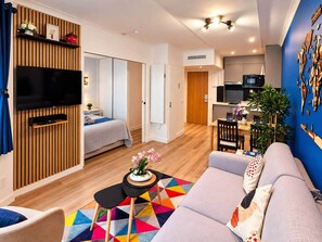 A modern living room with a sofa, a TV, and a dining area with a table and chairs. - Paris Expo 5 min – Cozy 1BR Apt with Balcony (Issy-les-Moulineaux)