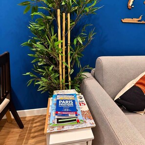 A room with a blue wall, a grey sofa, a small white table, and a bamboo plant. - Paris Expo 5 min – Cozy 1BR Apt with Balcony (Issy-les-Moulineaux)