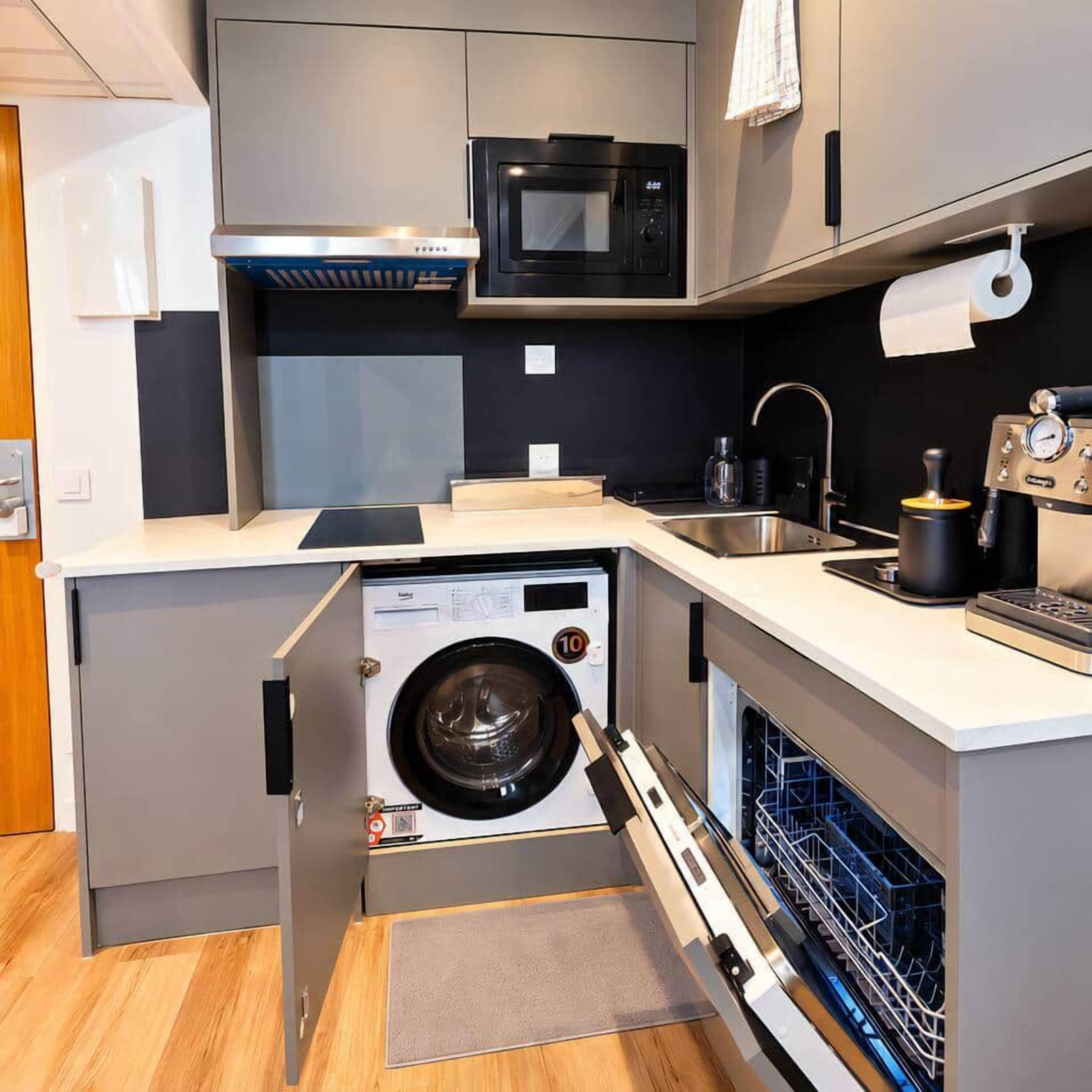 Een compacte keuken met een ingebouwde wasmachine, een magnetron en een koffiezetapparaat.