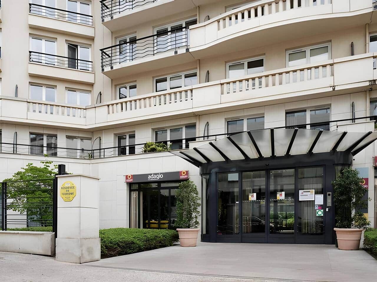 Un edificio de varios pisos con una entrada moderna que incluye una puerta de vidrio y un área de espera cubierta.