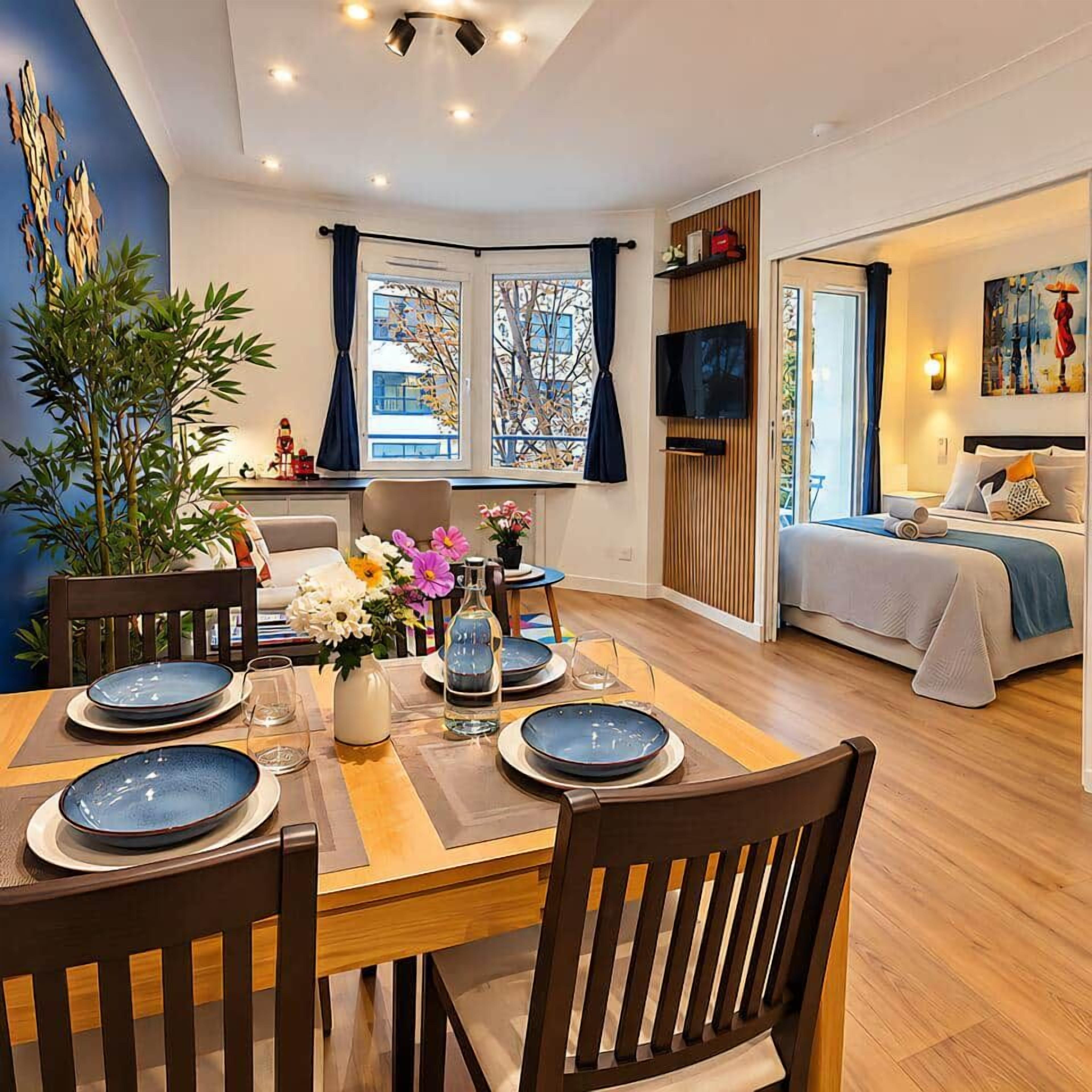 Un comedor moderno con una mesa de madera preparada para cuatro personas, una planta grande en maceta y vistas de la habitación.