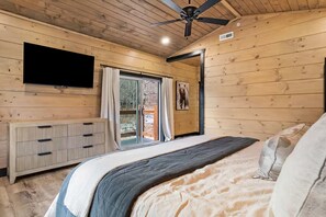 A bedroom with a bed, a television, a ceiling fan, and a sliding glass door leading to an outdoor area. - Heated Pool • Theater Room • Creekside Setting (Sevierville)