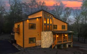 A two-story wooden house with a stone foundation, a porch, and multiple windows. - Heated Pool • Theater Room • Creekside Setting (Sevierville)