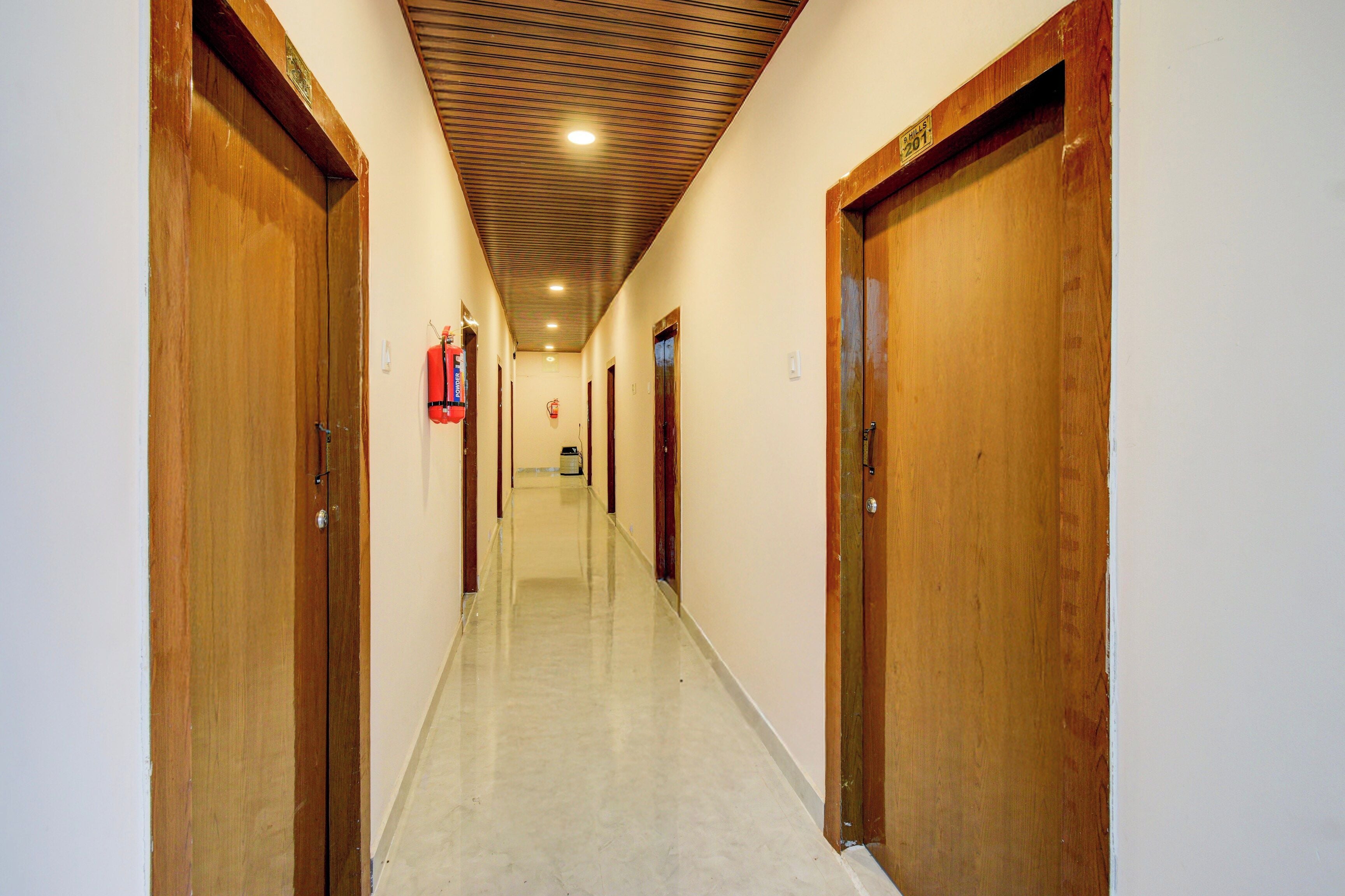 A hallway with wooden doors, a fire extinguisher, and a ceiling with a grid pattern.