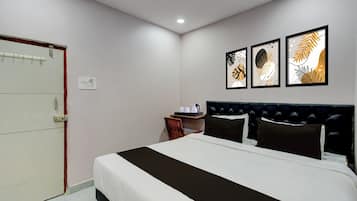 A hotel room with a bed, a bedside table with a kettle, and three framed artworks on the wall.