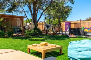 Un patio trasero con una mesa de madera, una hamaca y una zona de juegos con un mural colorido.