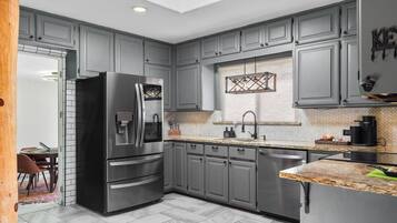 A modern kitchen with grey cabinets, a stainless steel refrigerator, a herringbone-patterned backsplash, and a skylight.