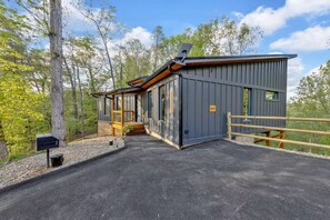 A modern cabin with a covered porch, a wooden deck, and a fenced driveway. - The W Retreat • Sauna • Hot Tub • 2 King Suites (Sevierville)