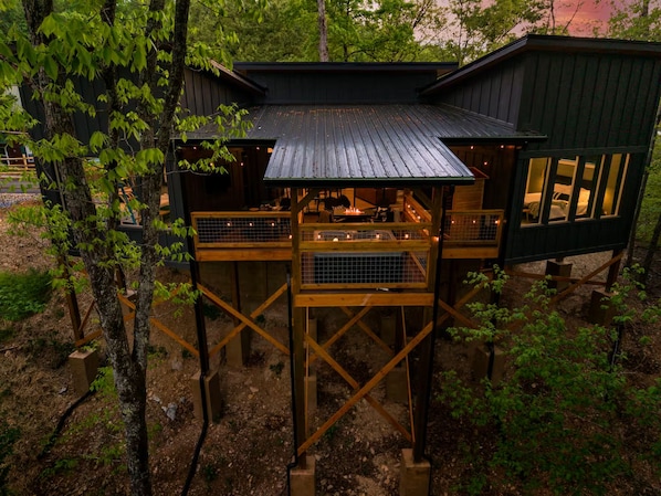 A treehouse with a wooden deck, a central open area with a fire pit, and a separate cabin-like structure. - The W Retreat • Sauna • Hot Tub • 2 King Suites (Sevierville)