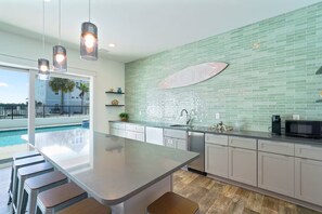 A modern kitchen with a large island, a built-in sink, and a view of a swimming pool. - Gulf Views-Pool-Beach 2 Min Walk-Hot Tub-Theatre (Santa Rosa Beach)