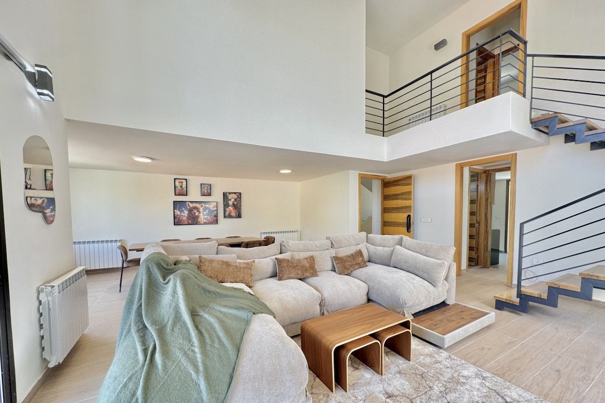 A spacious living area with a sectional sofa, a coffee table, and a staircase leading to an upper level.