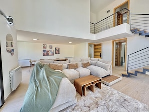 A spacious living area with a sectional sofa, a coffee table, and a staircase leading to an upper level. - Faqra Chalets by Stayinn (Faqra)