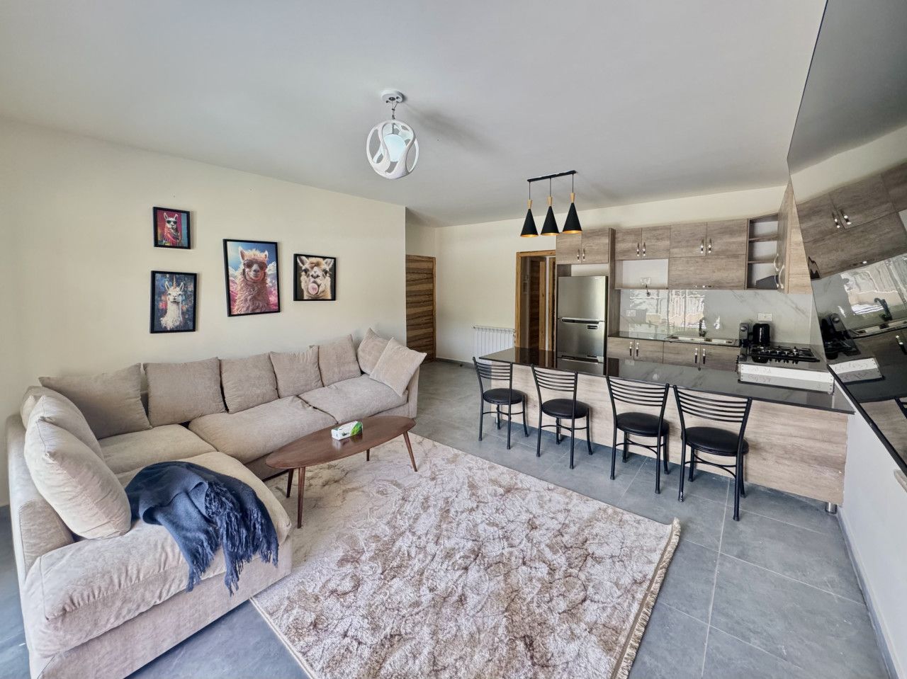 A modern living room with a sofa, coffee table, and a rug. There is a dining area with chairs and a kitchen with a stove and cabinets.