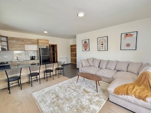 A modern living room with a sofa, coffee table, and chairs. There is a kitchen area with cabinets and appliances. - Faqra Chalets by Stayinn (Faqra)
