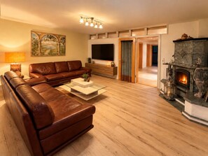 Ein Wohnzimmer mit braunem Ledersofa, einem Glastisch, einem Flachbildfernseher und einem Kamin.