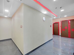 A hallway with a clock, emergency exit signs, and lockers.