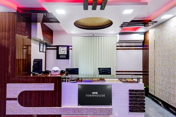 A reception desk with a digital clock, a computer, and a sign reading 'OYO TOWNHOUSE'.