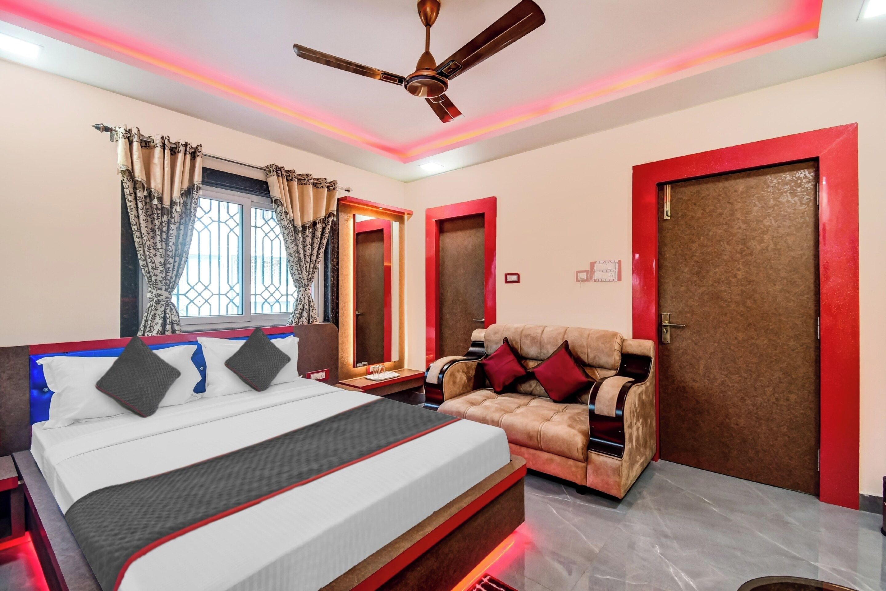 A hotel room with a bed, a sofa, a ceiling fan, and a window with curtains.