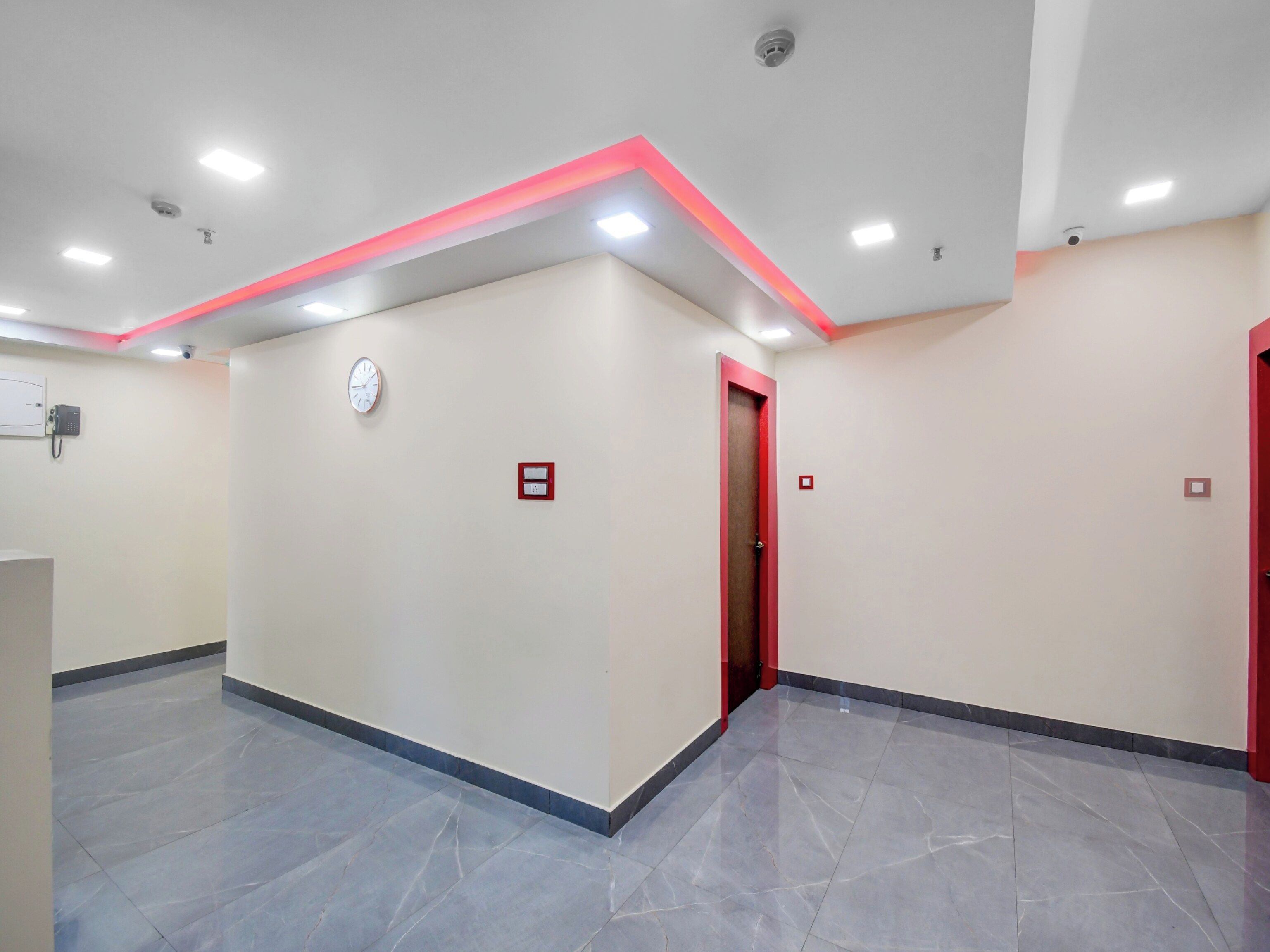 A spacious hallway with a clock, emergency buttons, and a red-framed door.