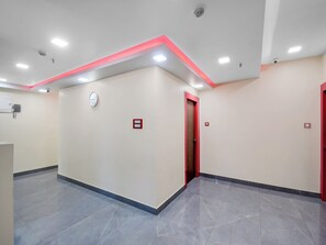 A spacious hallway with a clock, emergency buttons, and a red-framed door. - Hotel O THE CROWN COMFORTS (Bidhannagar)