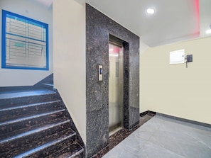 A modern elevator with a digital display, a staircase with dark marble steps, and a wall-mounted phone.