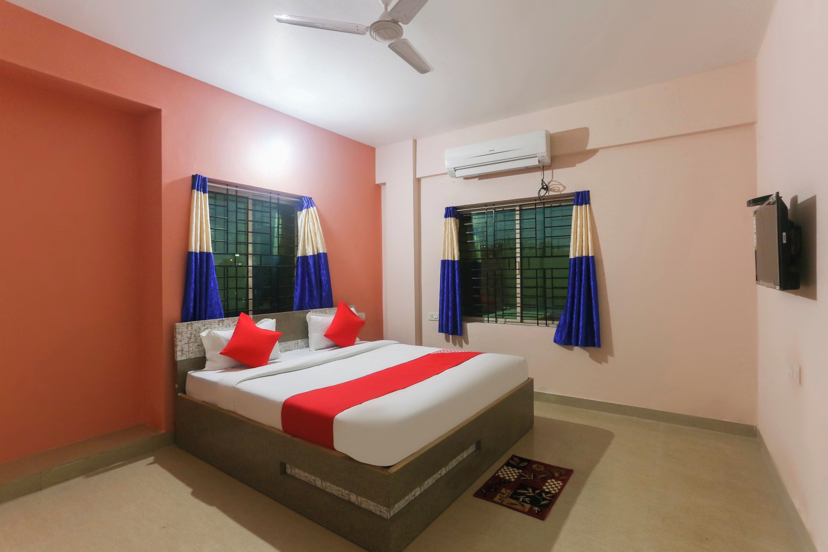 A bedroom with a bed, two windows with curtains, an air conditioning unit, and a ceiling fan.