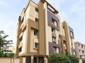 Un edificio residencial de varios pisos con un diseño arquitectónico moderno, que combina tonos beige y marrones, y un techo plano.