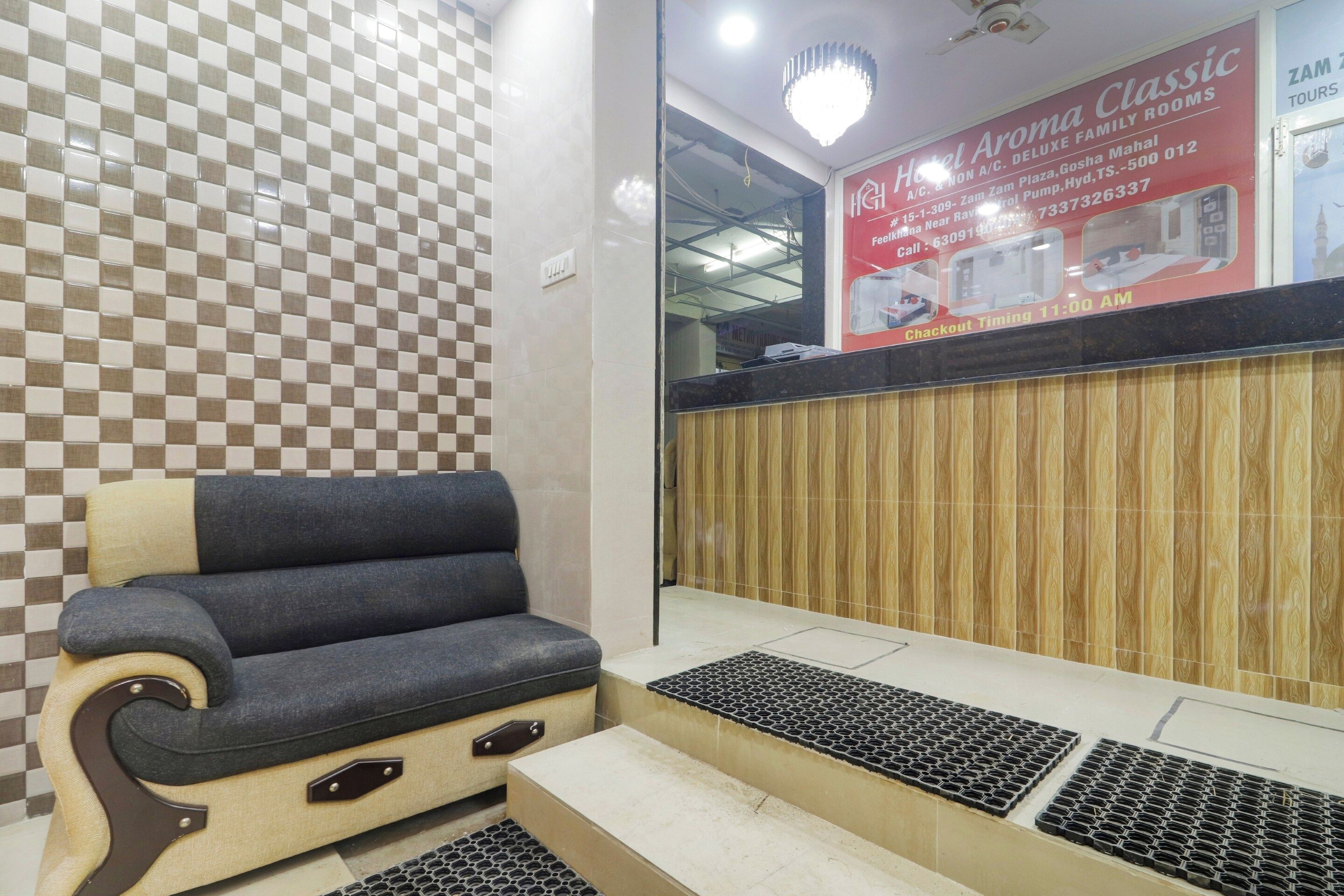 Zona de recepción de un hotel con un estampado de cuadros en la pared, un mostrador de recepción, un área de estar con una silla acolchada y un panel de pared de madera.