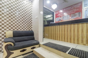 A hotel reception area with a checkered wall pattern, a reception desk, a seating area with a cushioned chair, and a wooden panel wall.
