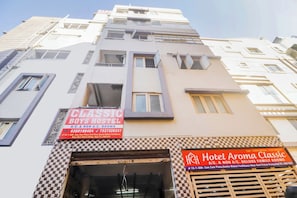 Um edifício de vários andares com placas indicando 'CLASSIC BOYS HOSTEL' e 'Hotel Aroma Classic', mostrando que há quartos com e sem ar condicionado.