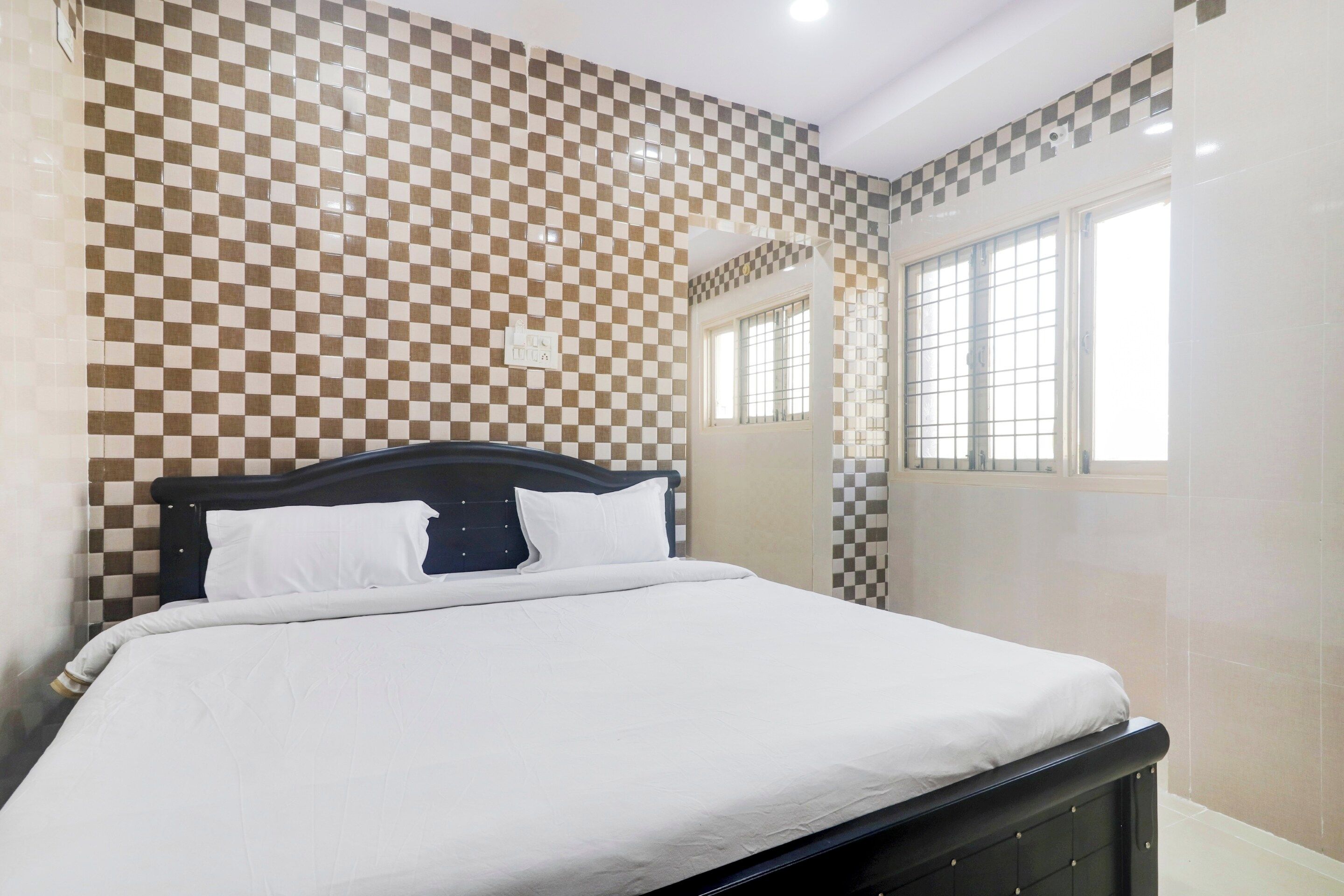 Un dormitorio con un estampado de cuadros en la pared, una cama con ropa blanca y un ventanal con vistas.